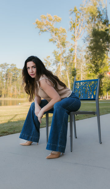 Woman sitting on a chair outdoors with trees and grass in the background. Stockbridge Styles Judy blue jeans and Stockbridge Styles sweater knit top