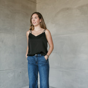 Woman wearing Stockbridge Styles black top and Judy blue jeans standing against a plain wall. shop stockbridge styles
