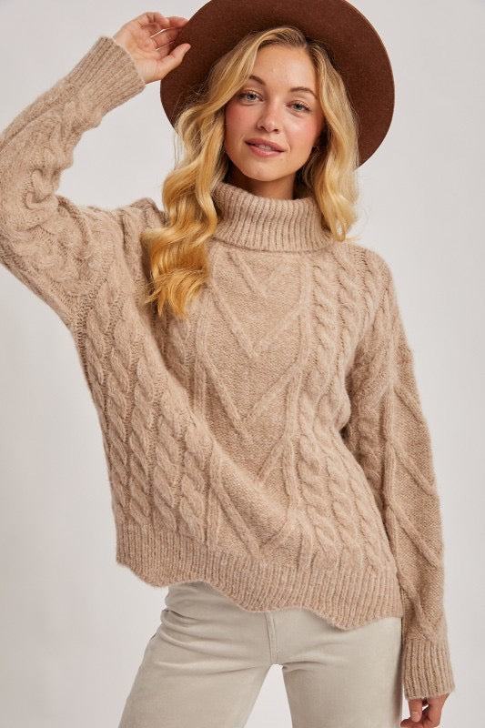 Woman wearing a beige cable knit sweater and brown hat on a white background