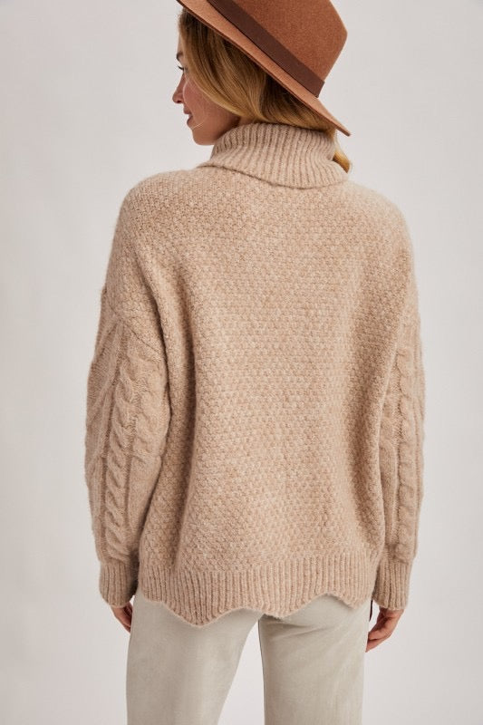 Person wearing a beige knitted sweater and brown hat on a plain background