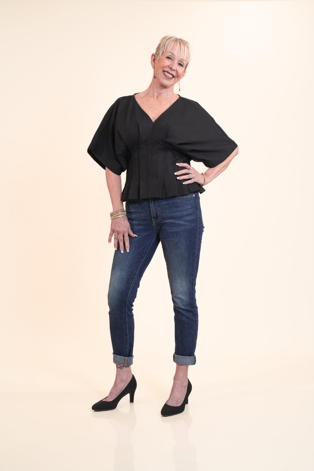 Woman wearing a black top and blue jeans on a beige background