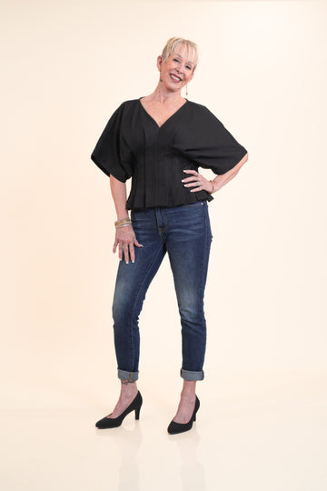 Woman wearing a black top and blue jeans on a beige background