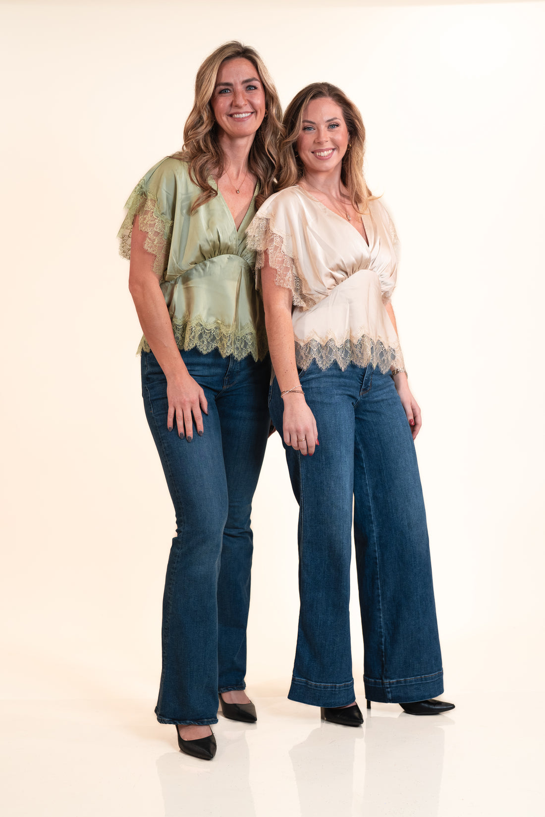 Two women wearing matching outfits with lace tops and blue jeans on a white background