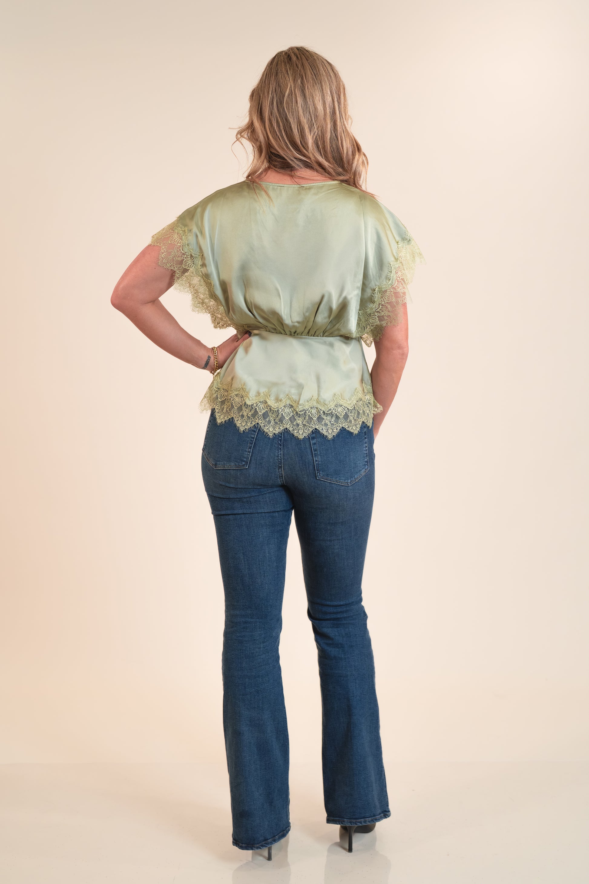 Woman wearing a green lace top and blue jeans on a beige background