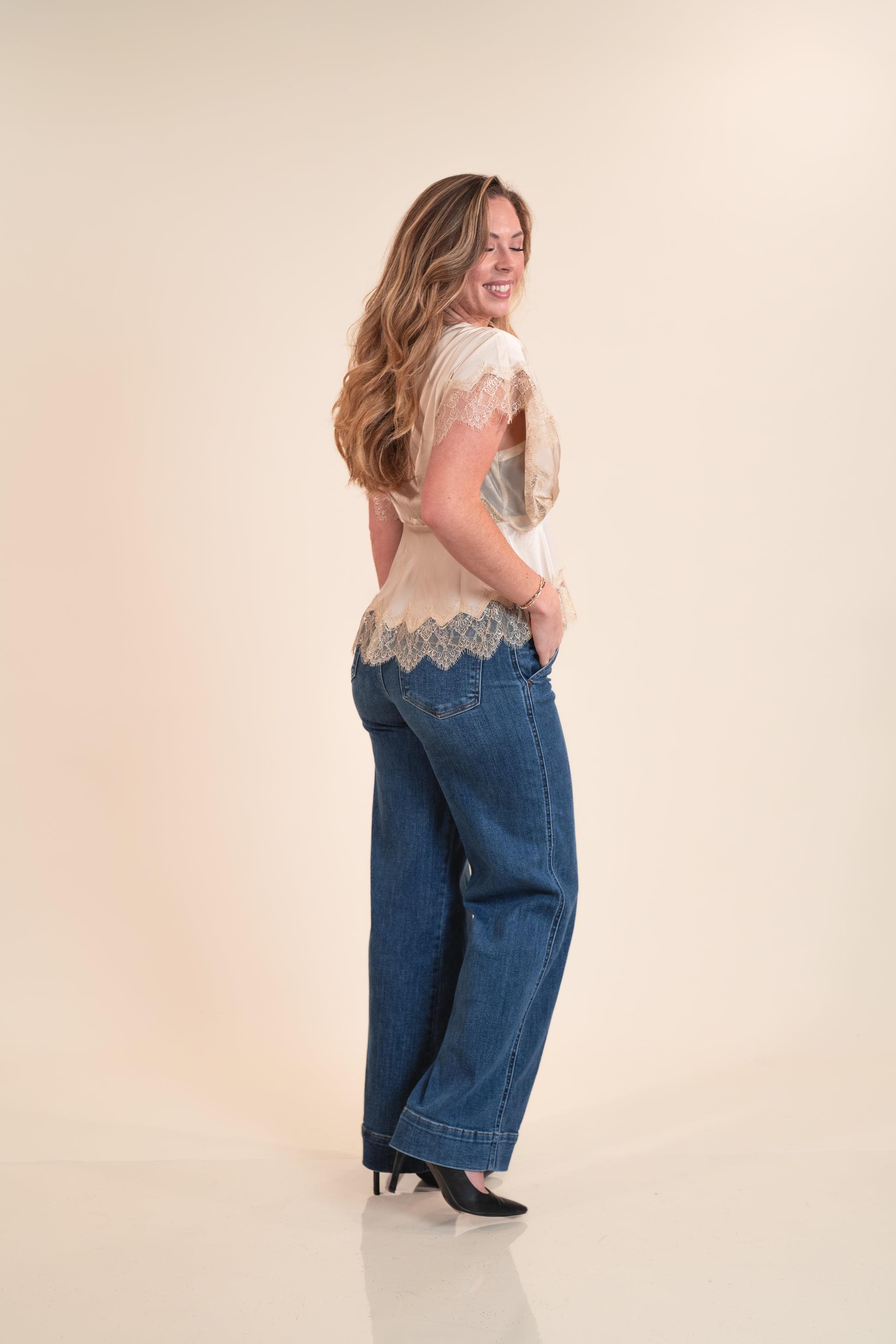 Woman wearing a lace top and blue jeans on a beige background