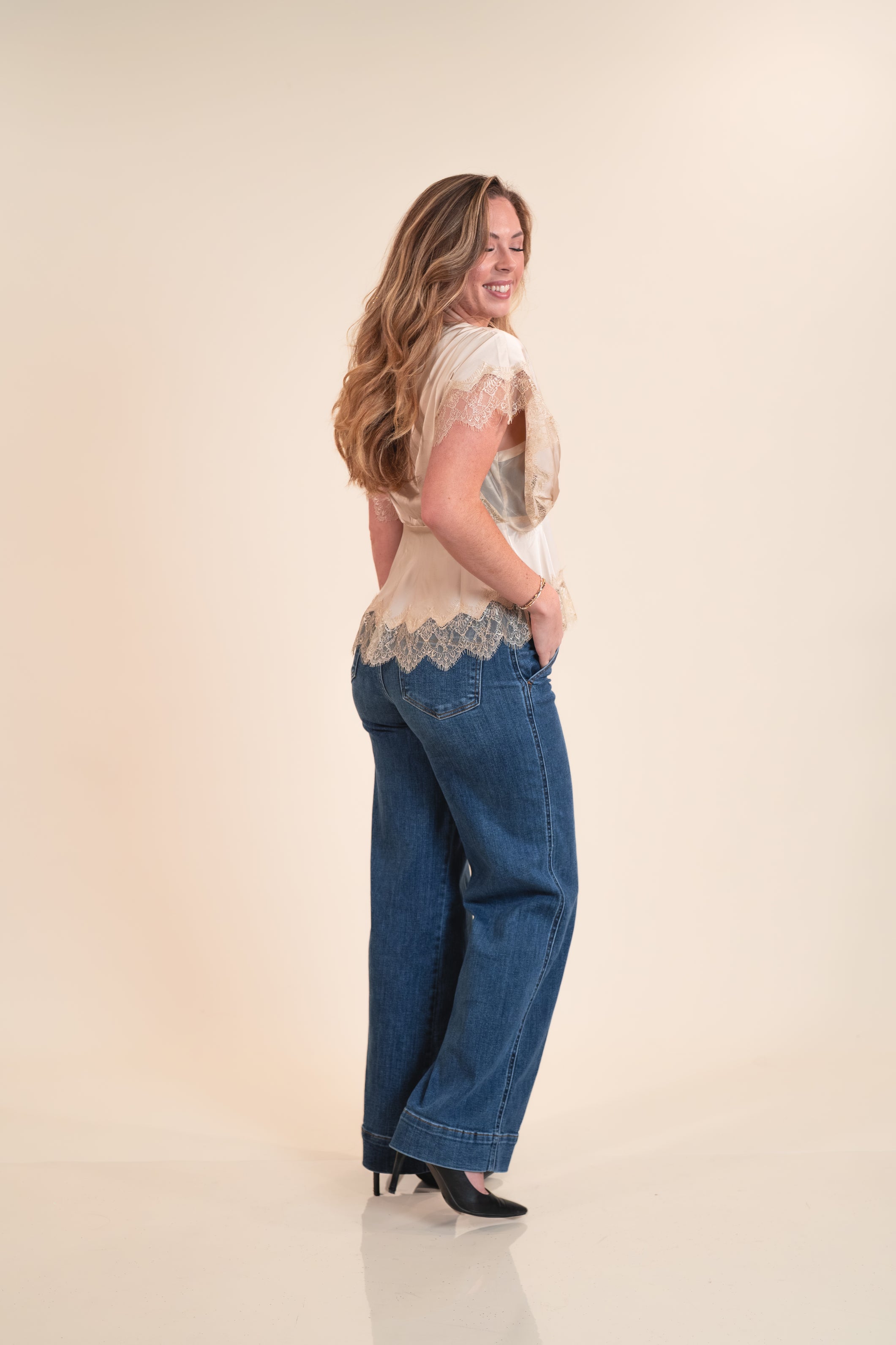 Woman wearing a lace top and blue jeans on a beige background