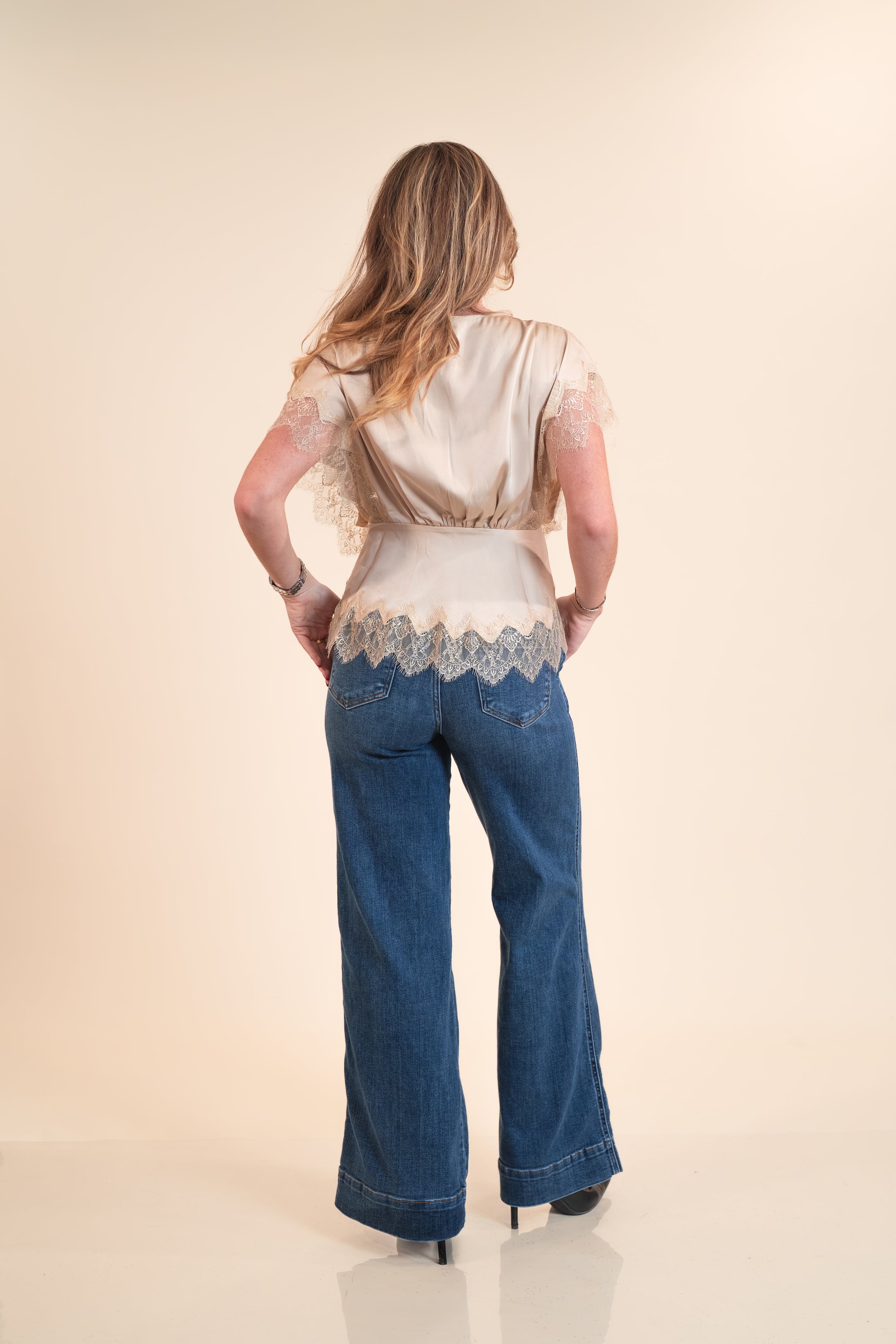 Woman wearing a lace top and blue jeans on a beige background
