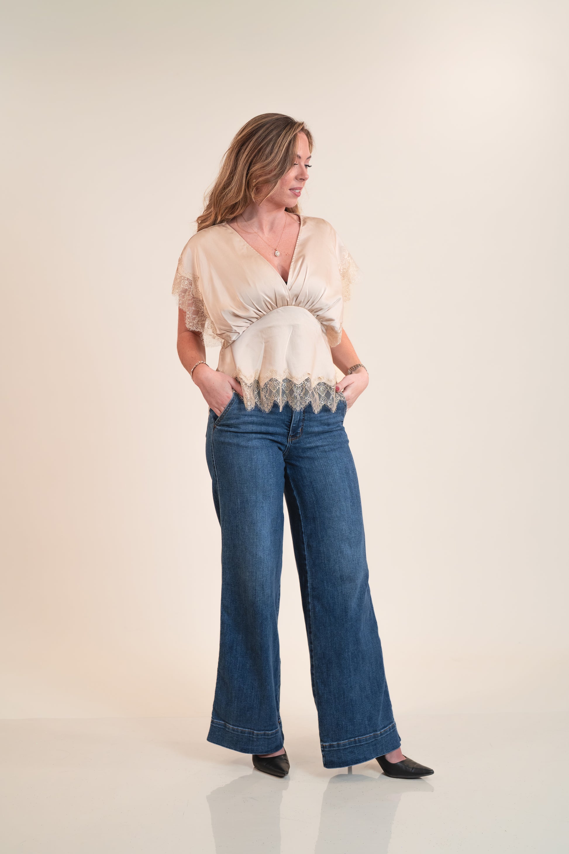 Woman wearing a beige blouse with lace details and blue jeans on a white background