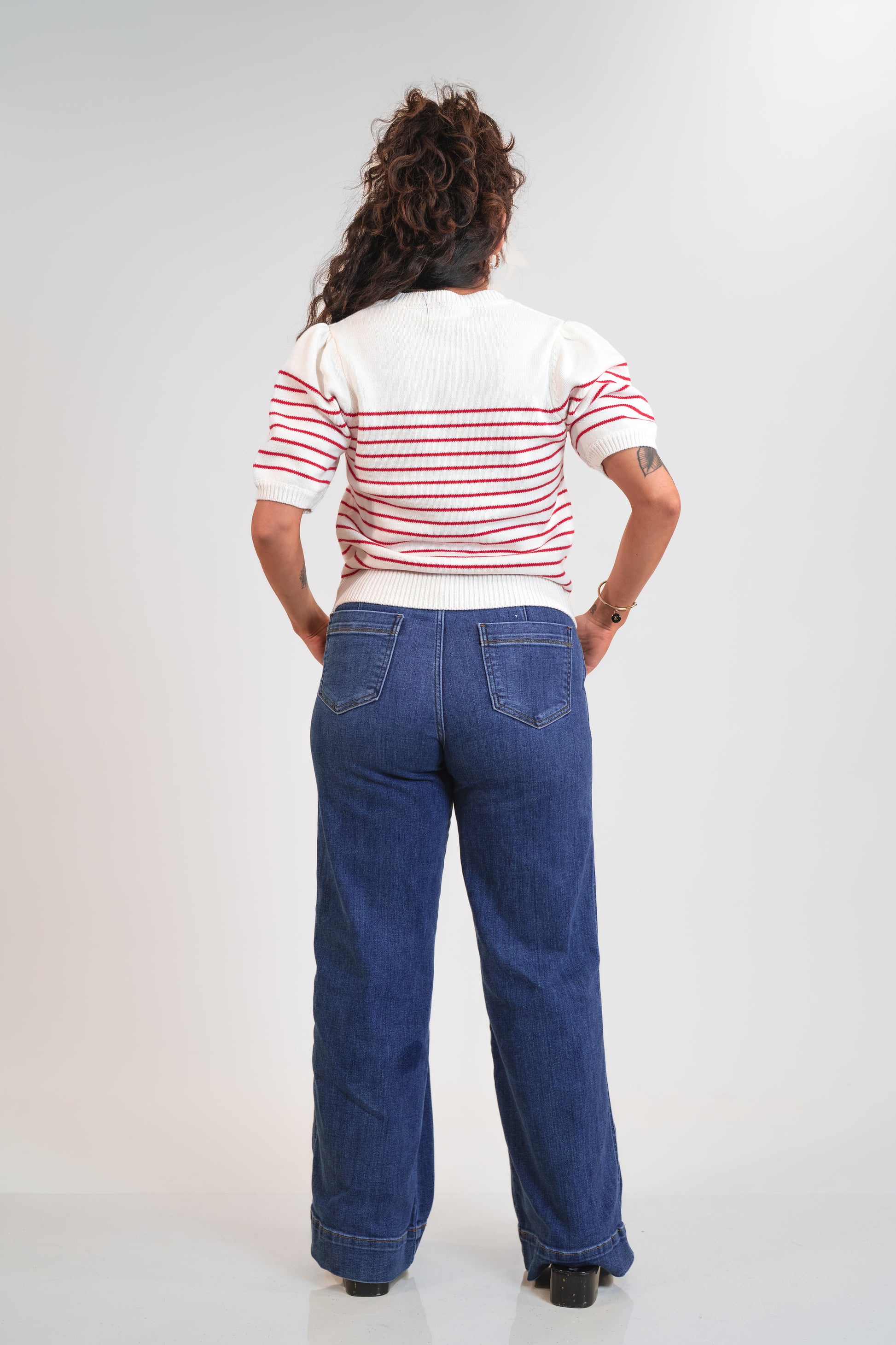 Person wearing a striped shirt and blue jeans from behind on a white background