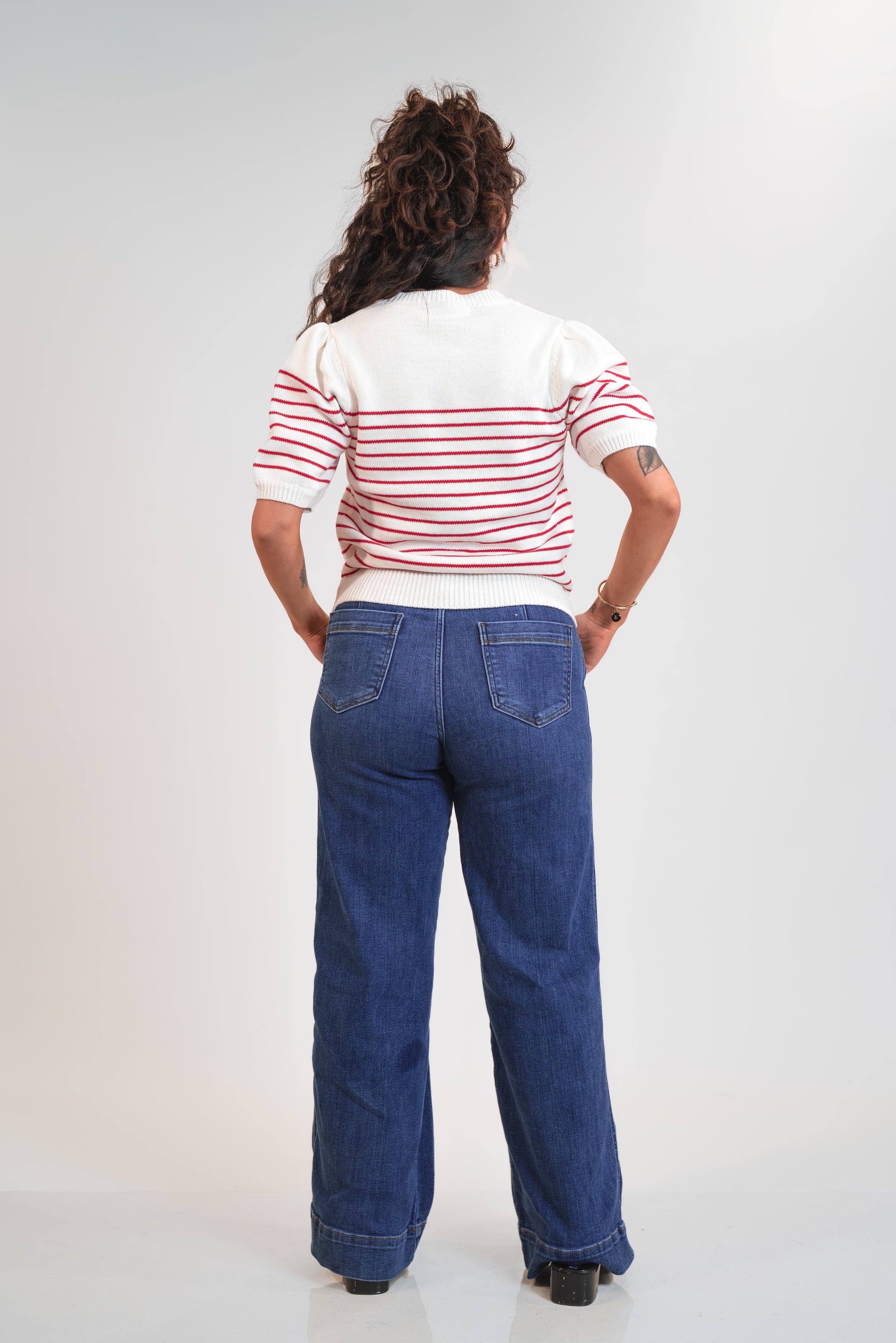 Person wearing a striped shirt and blue jeans from behind on a white background