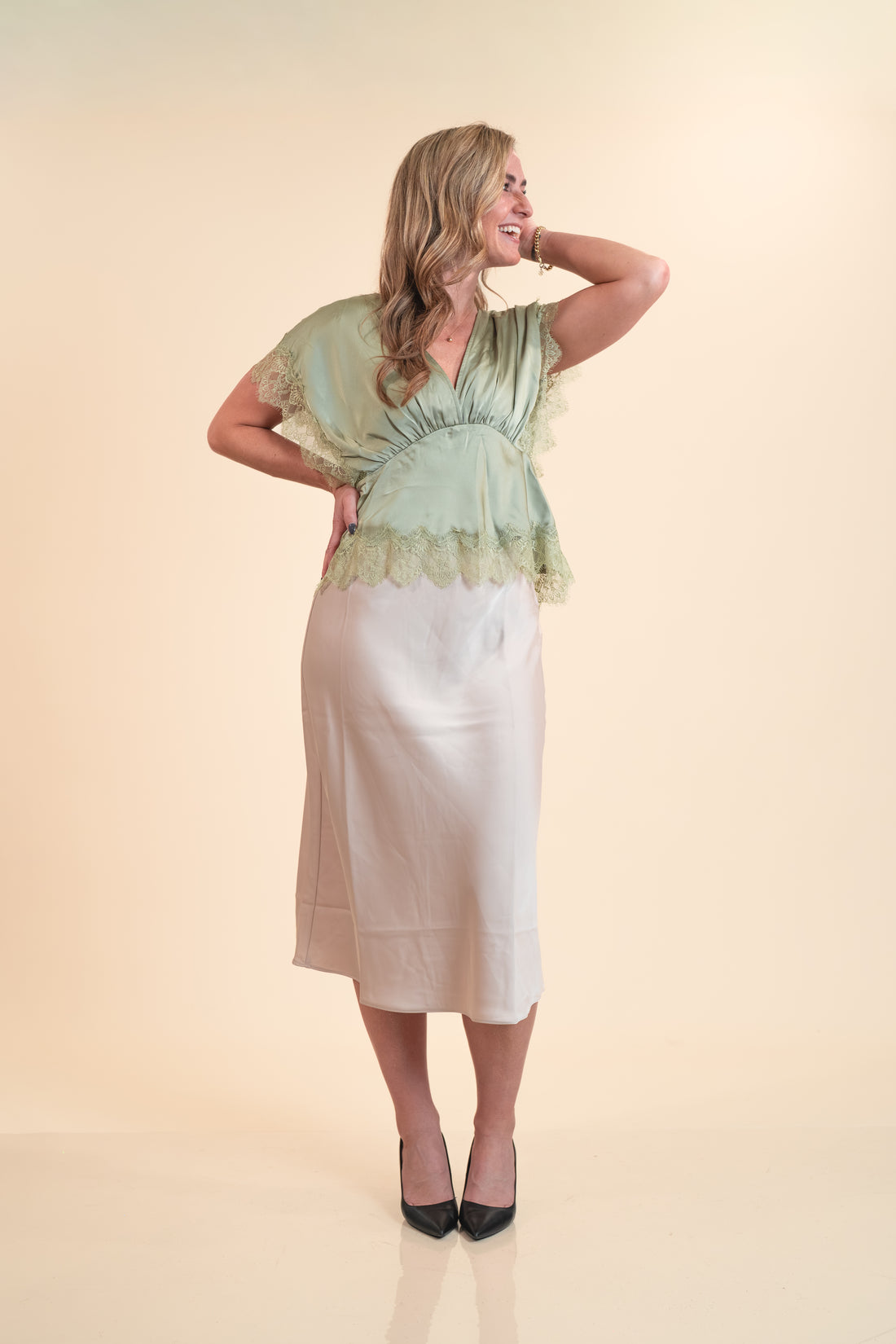 Woman wearing a light green top and white skirt on a beige background