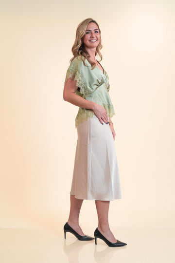 Woman wearing a light green top and white skirt on a beige background