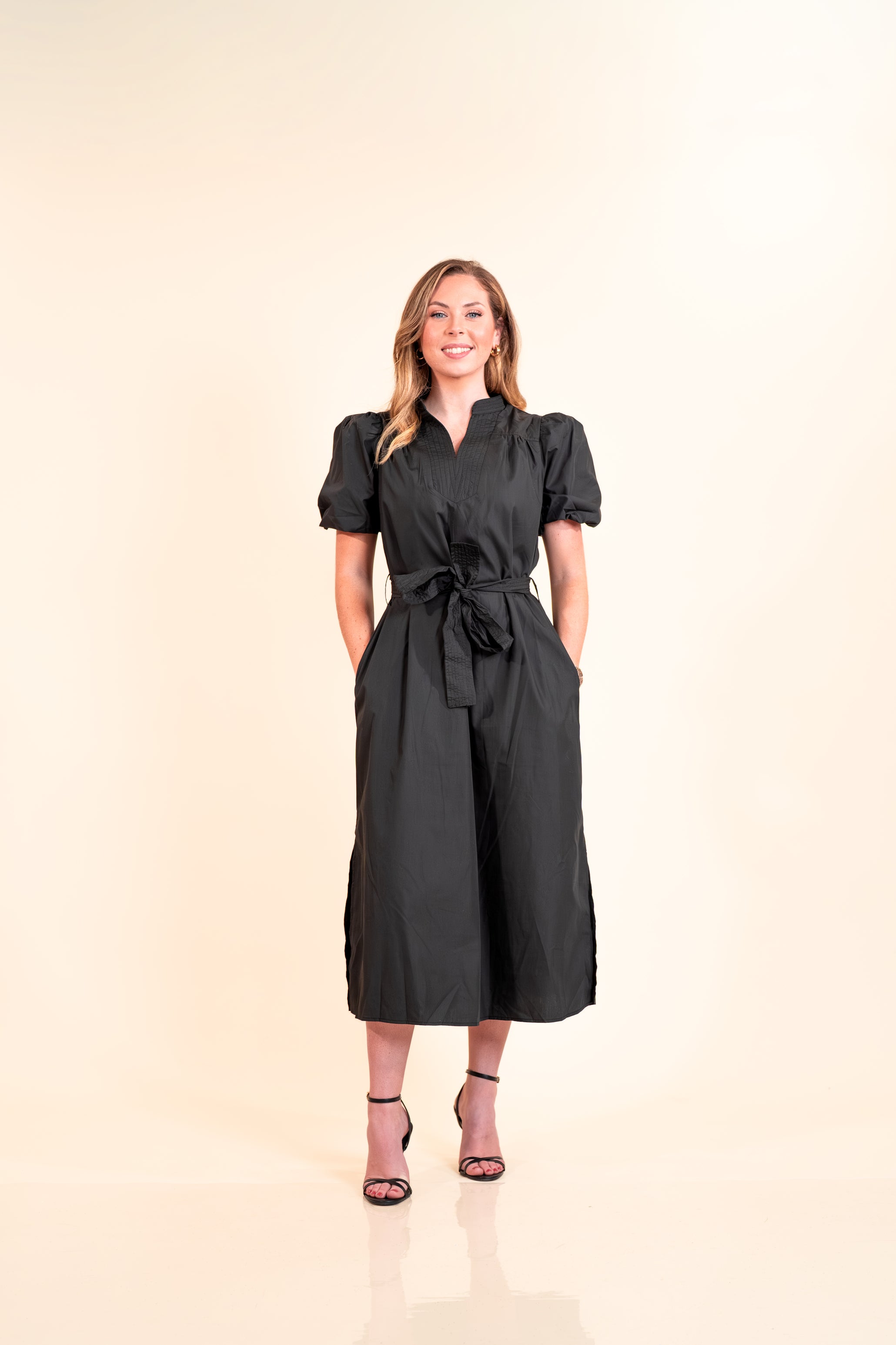 Woman wearing a black dress with puff sleeves on a beige background