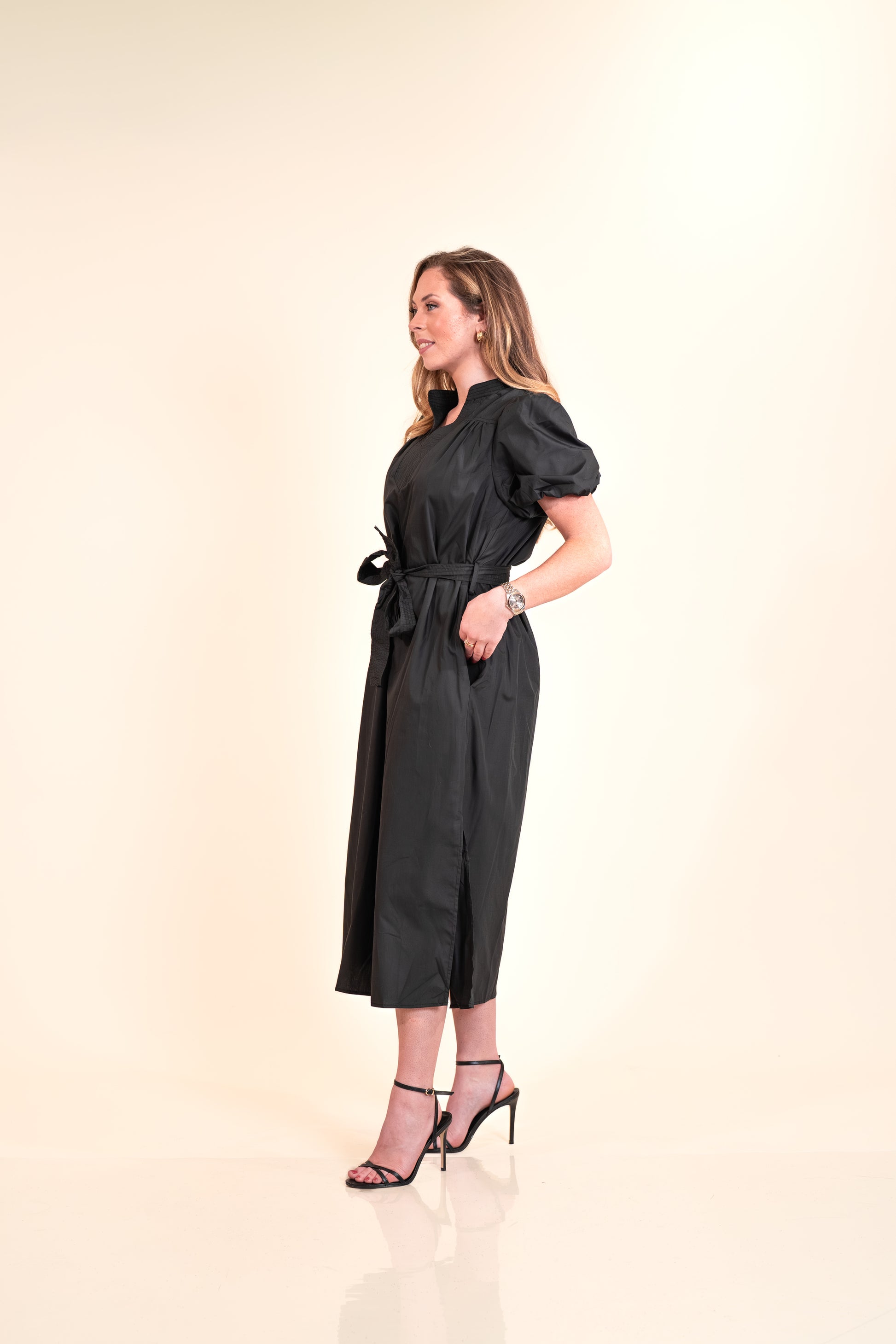 Woman wearing a black dress standing against a beige background