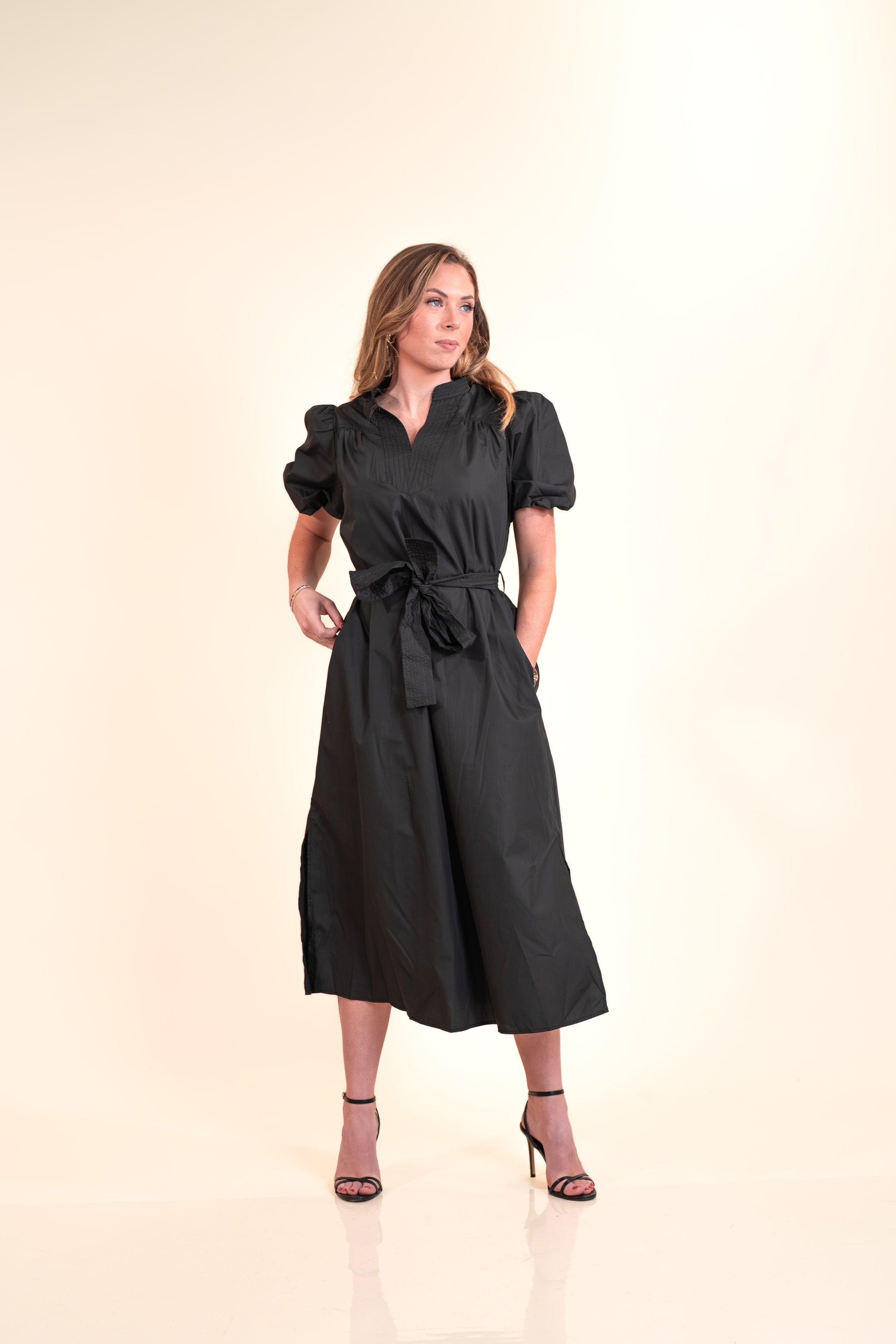 Woman wearing a black dress with puff sleeves on a beige background