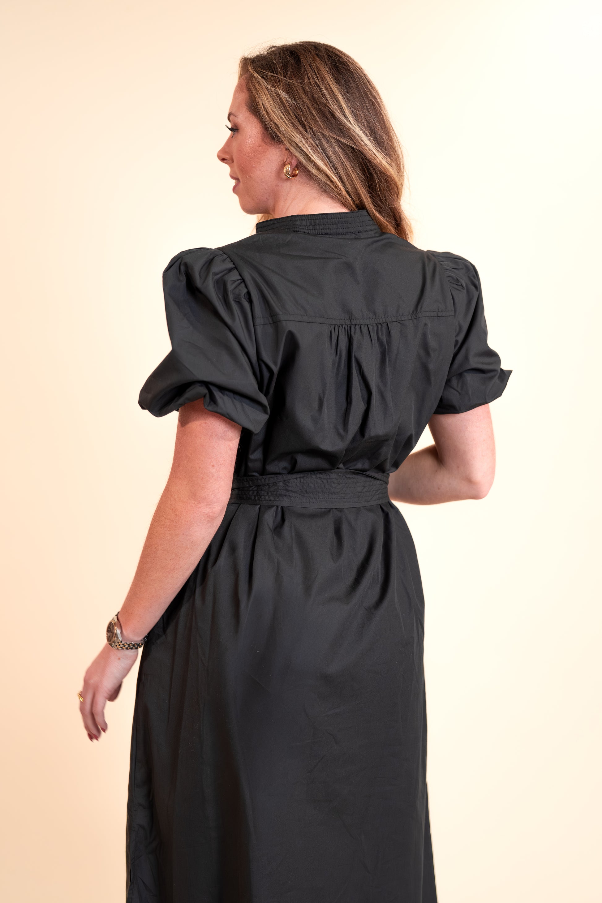 Woman wearing a black dress with puffed sleeves on a beige background