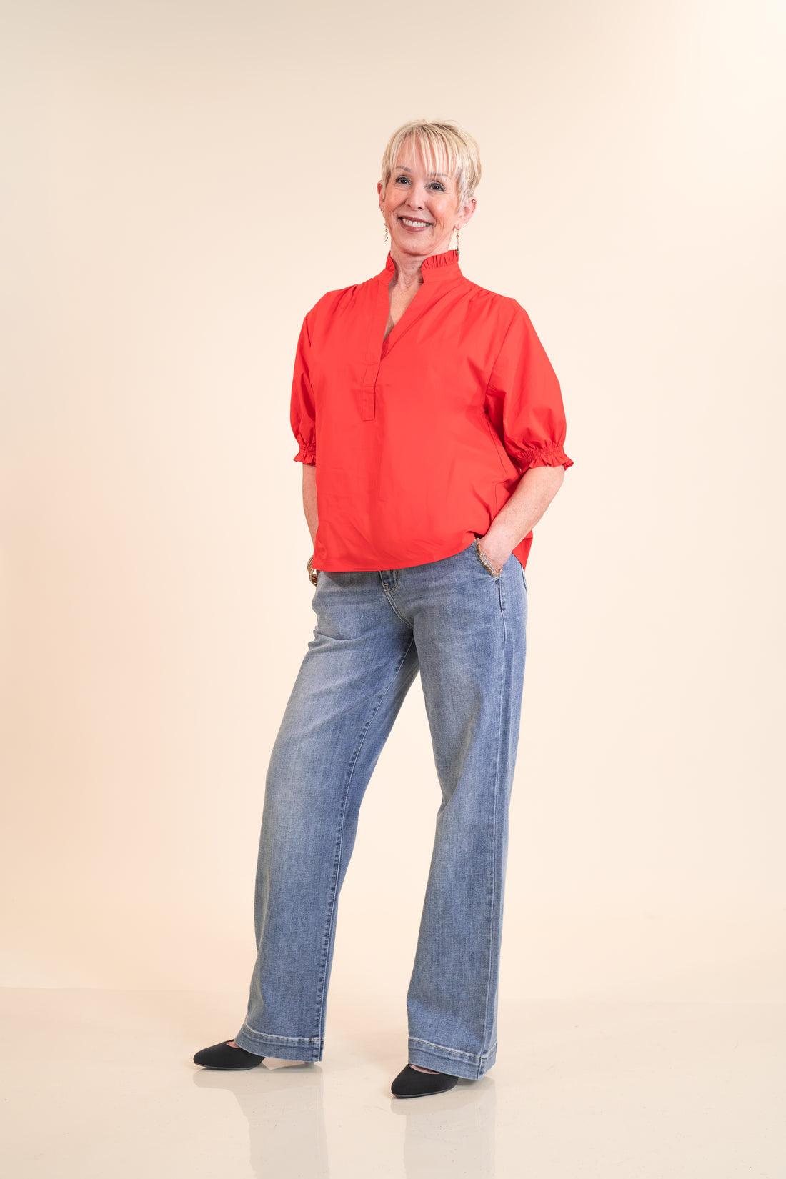 Woman wearing a red blouse and blue jeans against a beige background