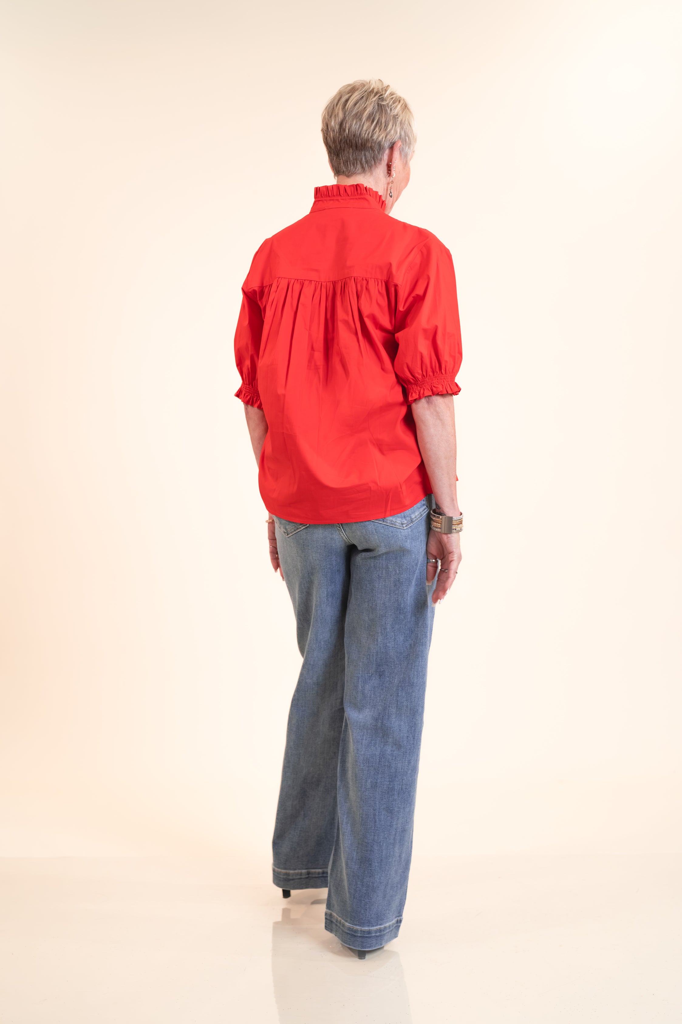 Person wearing a red blouse and blue jeans from behind on a beige background