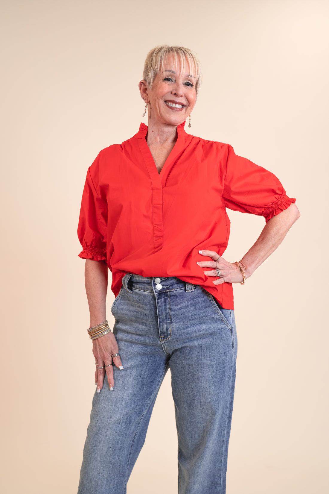 Woman wearing a red blouse and blue jeans against a beige background
