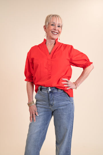 Woman wearing a red blouse and blue jeans against a beige background