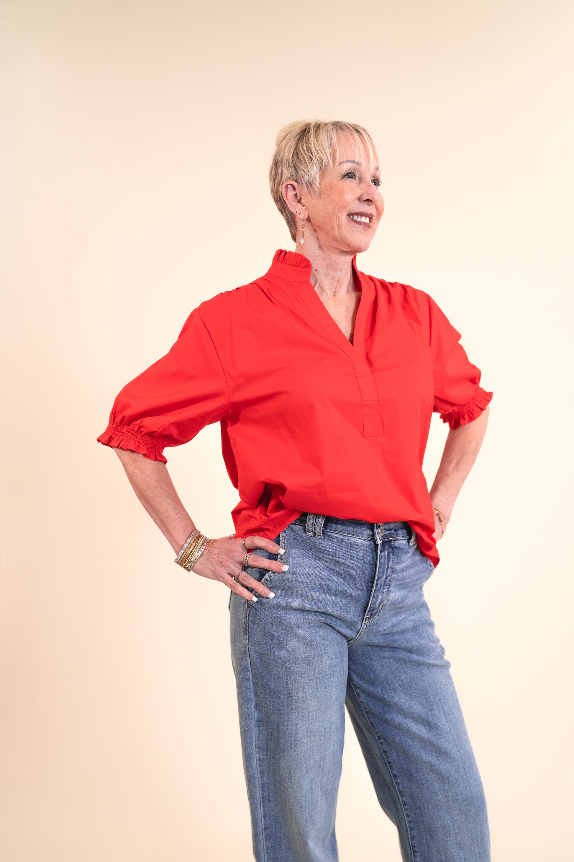 Woman wearing a red blouse and blue jeans on a beige background
