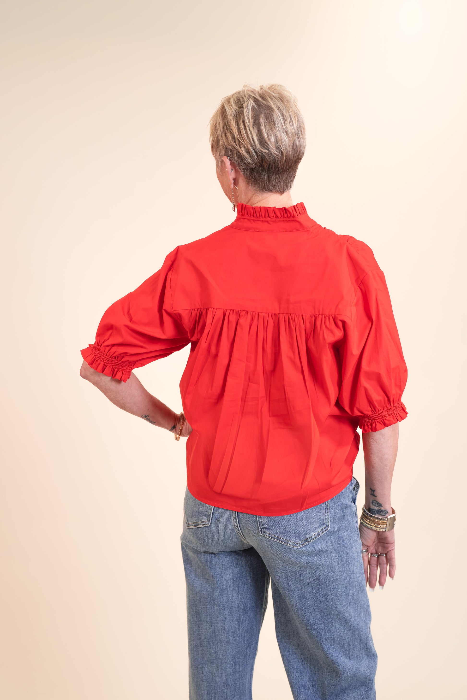 Person wearing a red blouse with puffed sleeves and blue jeans on a beige background