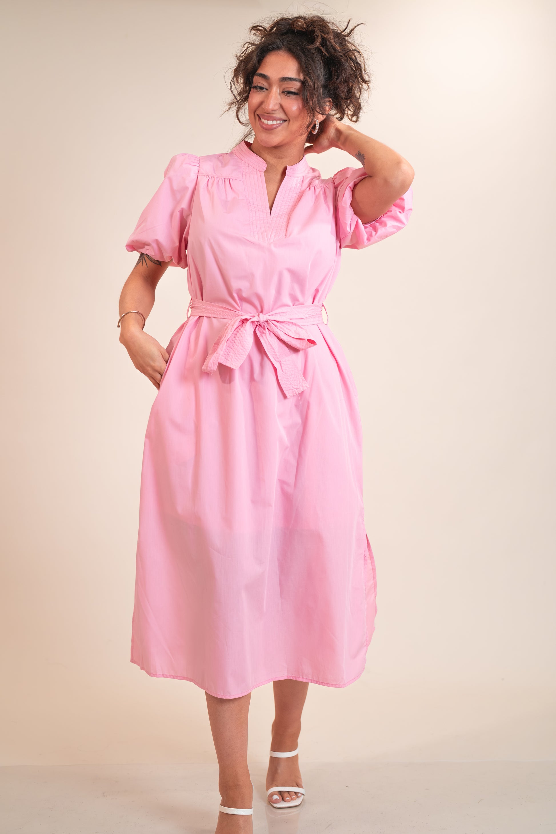 Woman wearing a pink dress with a belt on a beige background