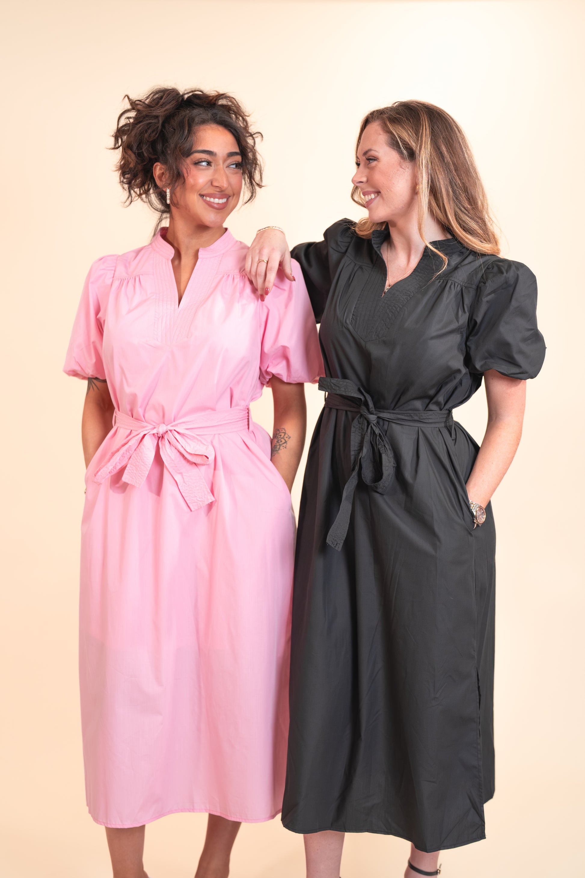 Two women wearing pink and black dresses against a beige background