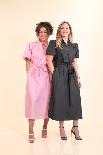 Two women wearing pink and black dresses standing against a beige background