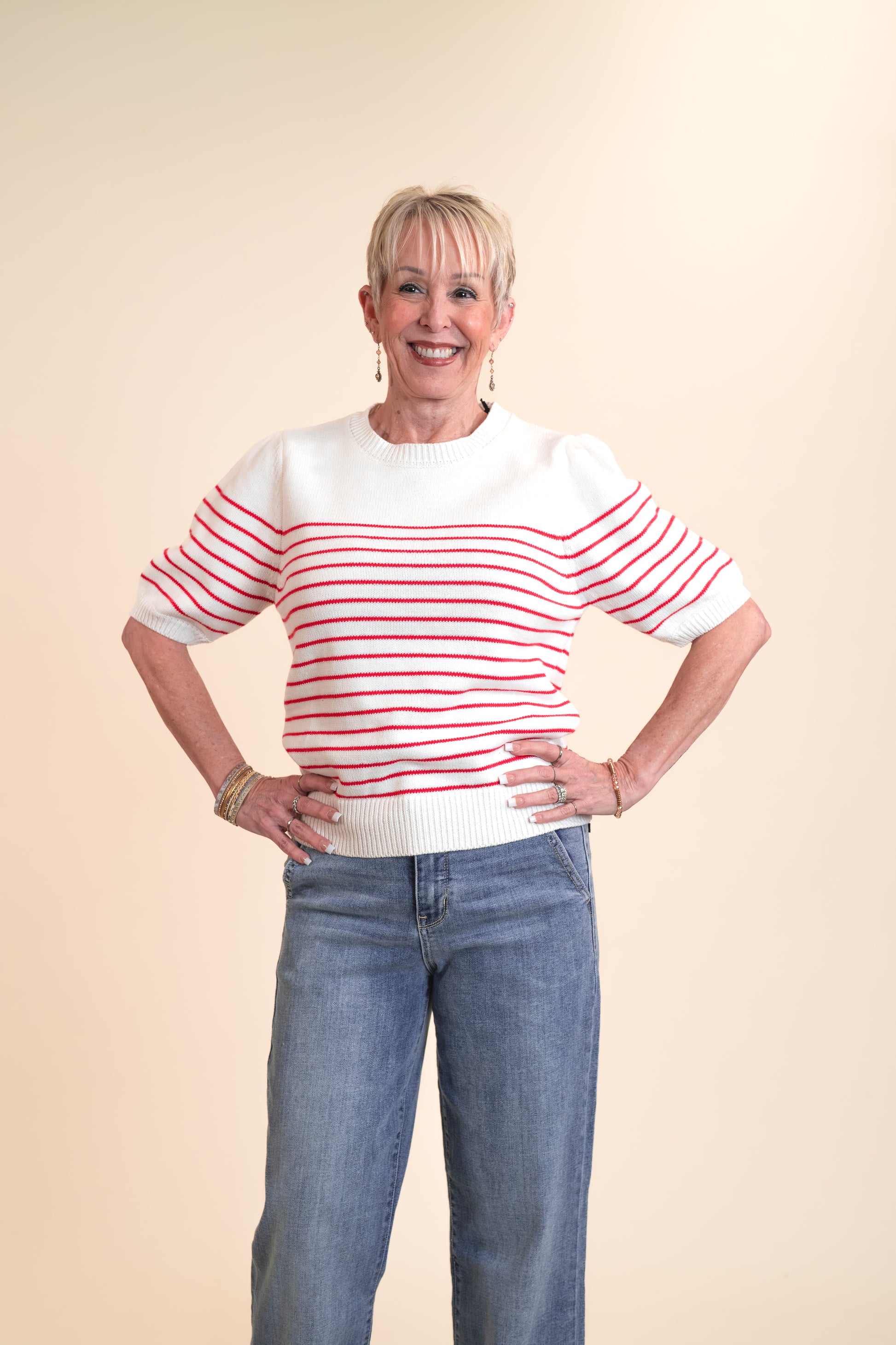 Woman wearing a red and white striped sweater and blue jeans on a beige background