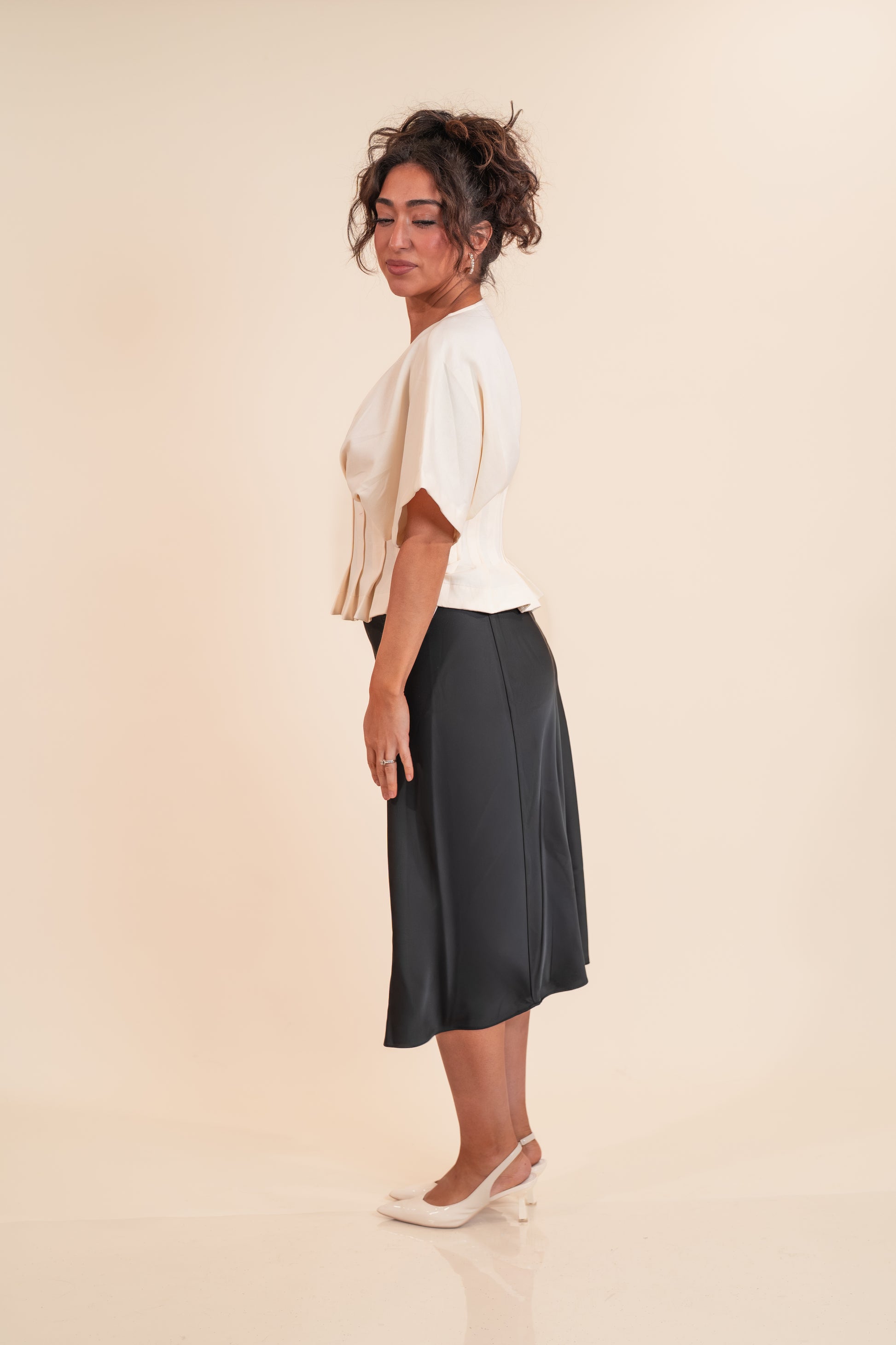 Woman wearing a white top and dark skirt on a beige background