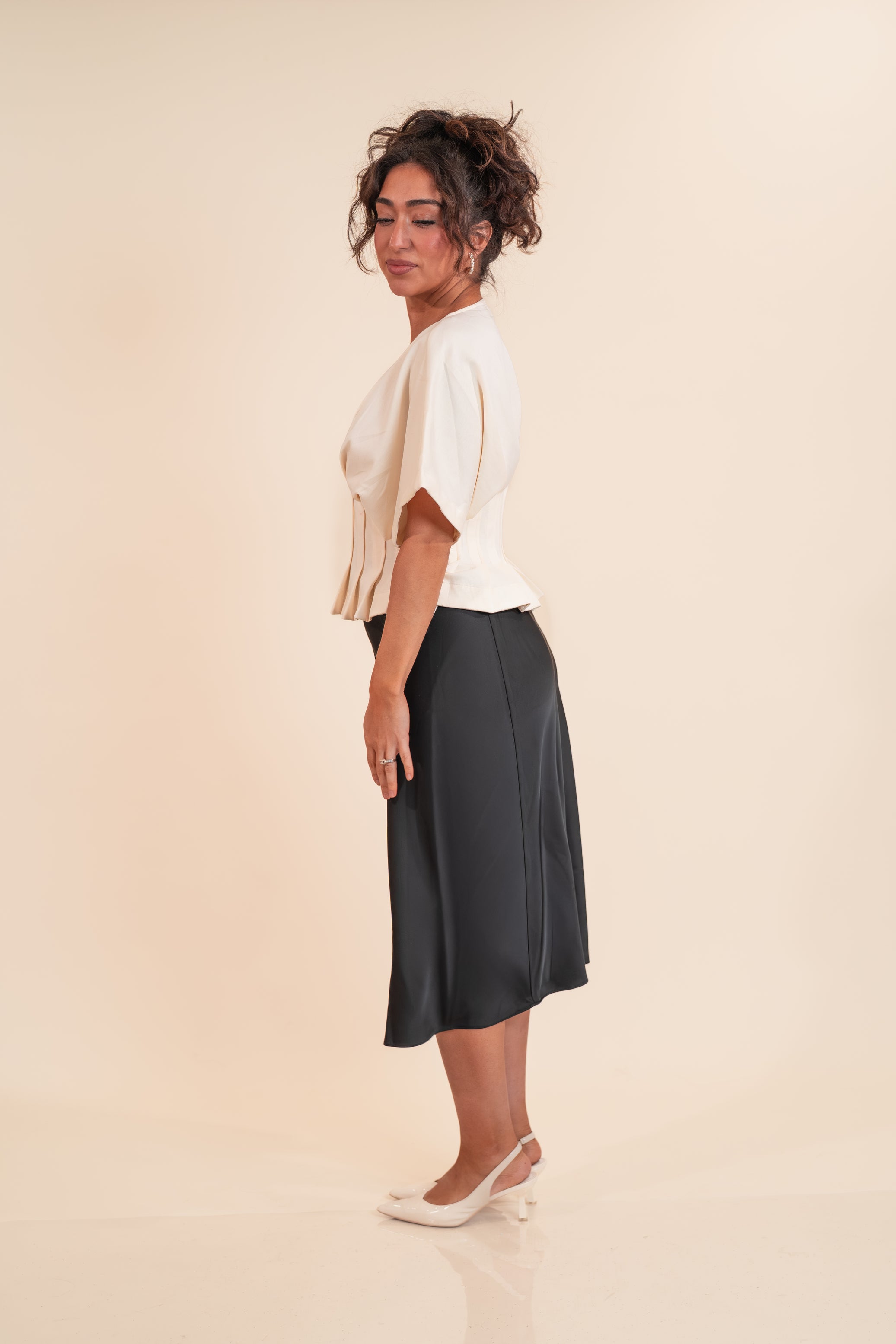 Woman wearing a white top and dark skirt on a beige background