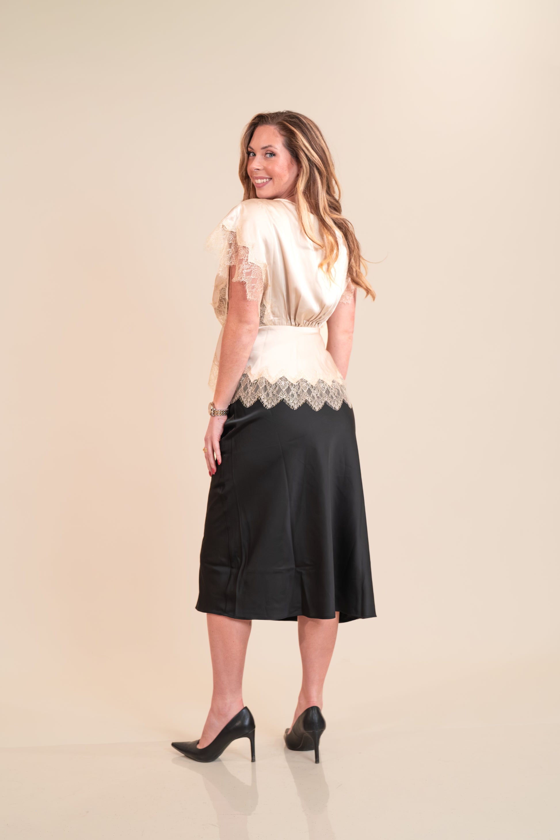 Woman wearing a black skirt and white top with lace details on a beige background