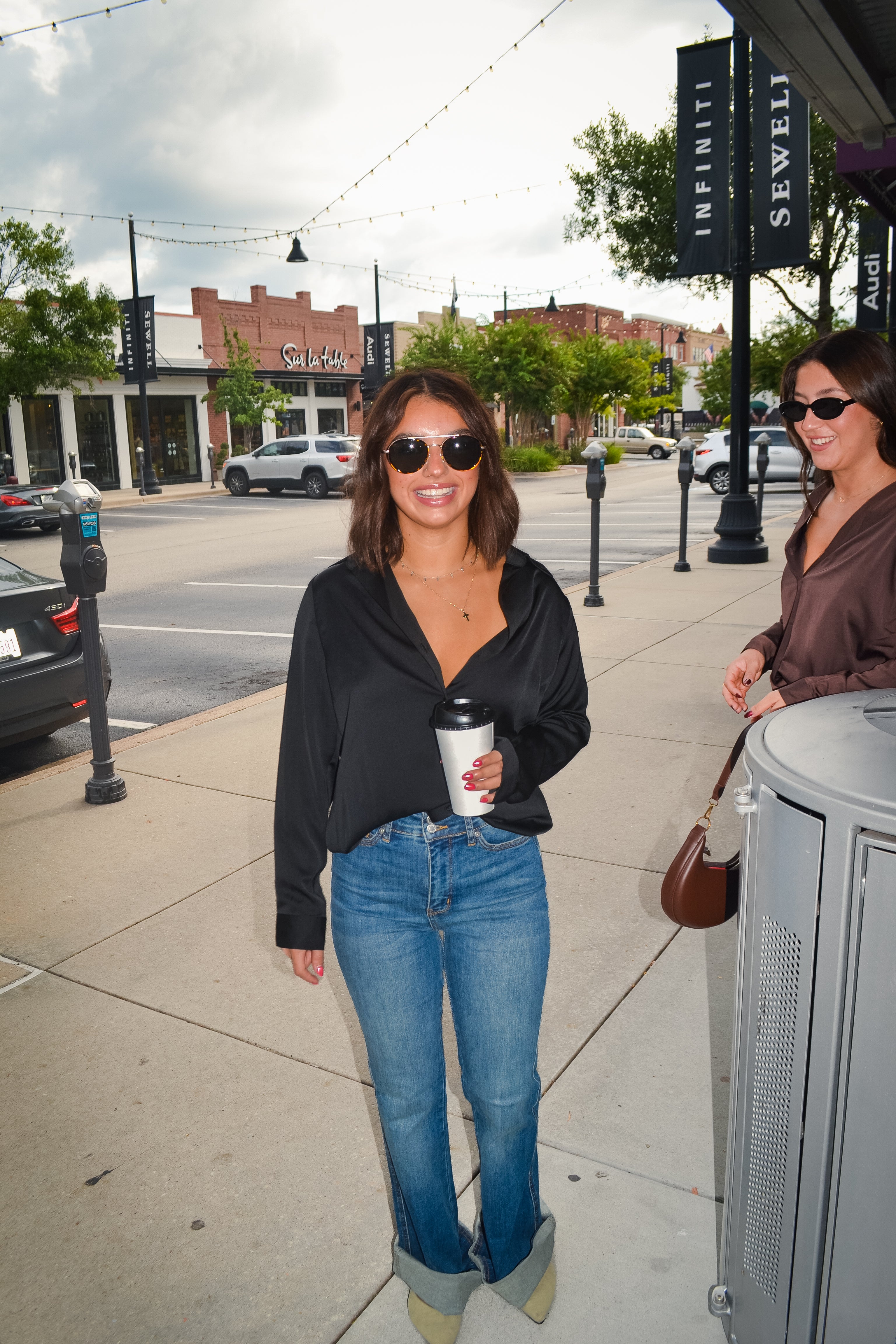 Woman walking on a sidewalk holding a coffee cup, with a city street background.
