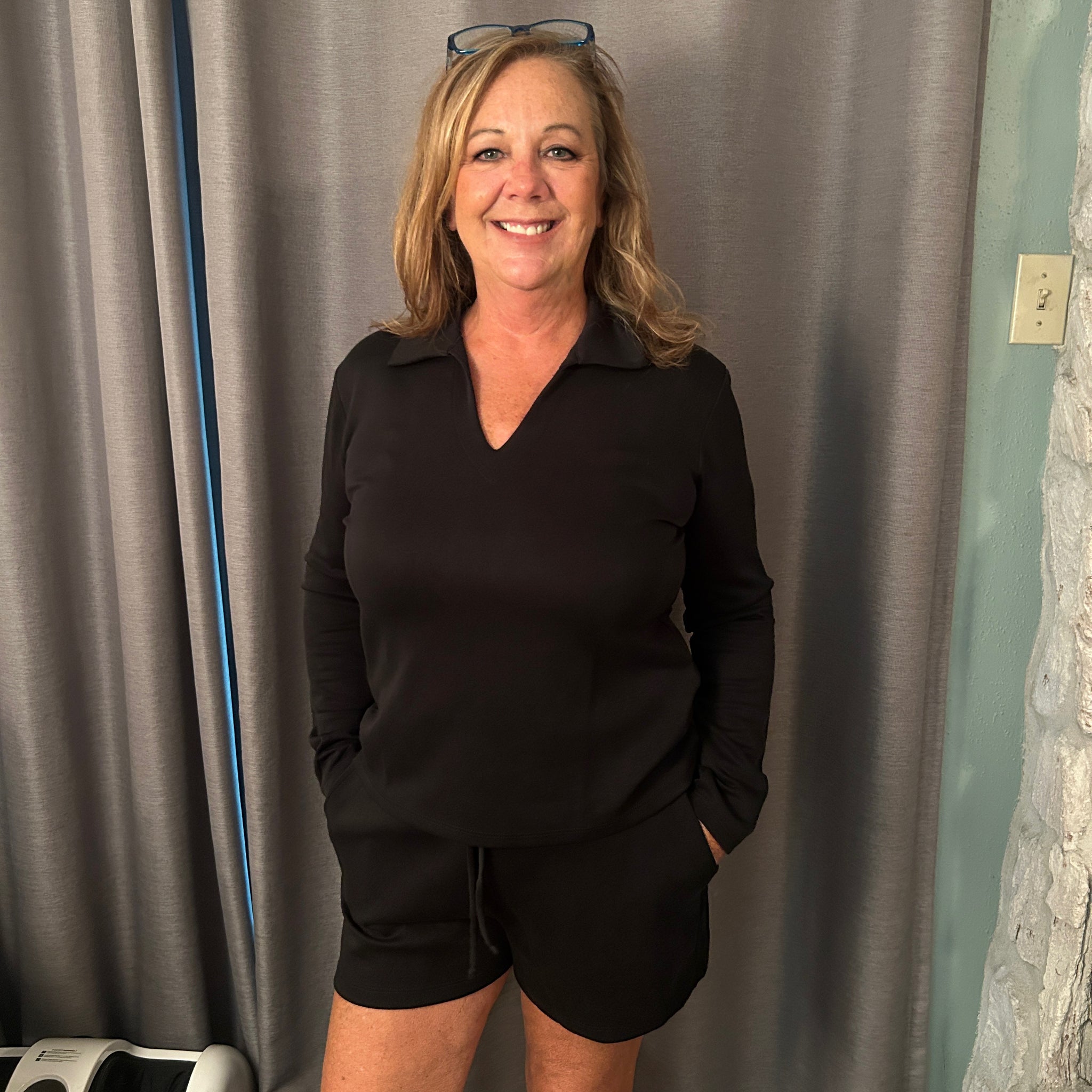 Woman wearing a black outfit standing in front of a gray curtain.