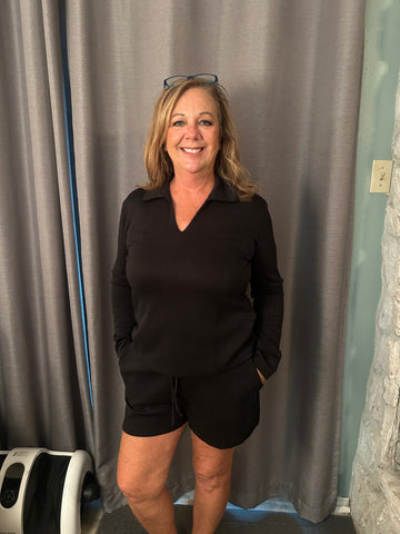 Woman wearing a black outfit standing in front of a gray curtain.