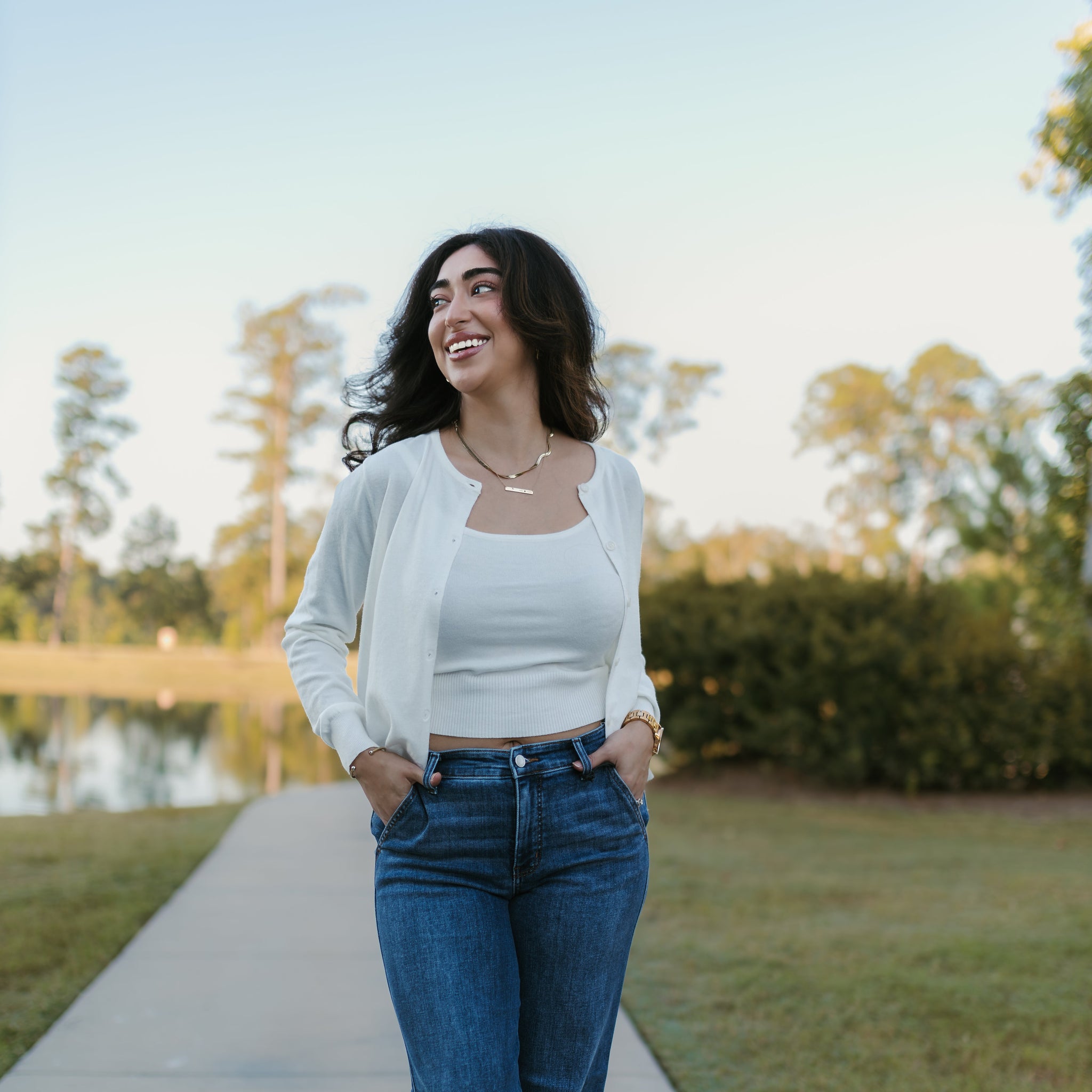 Woman walking on a path outdoors with trees and grass in the background. Stockbridge Styles cardigan set. Stockbridge Styles Judy blue jeans.