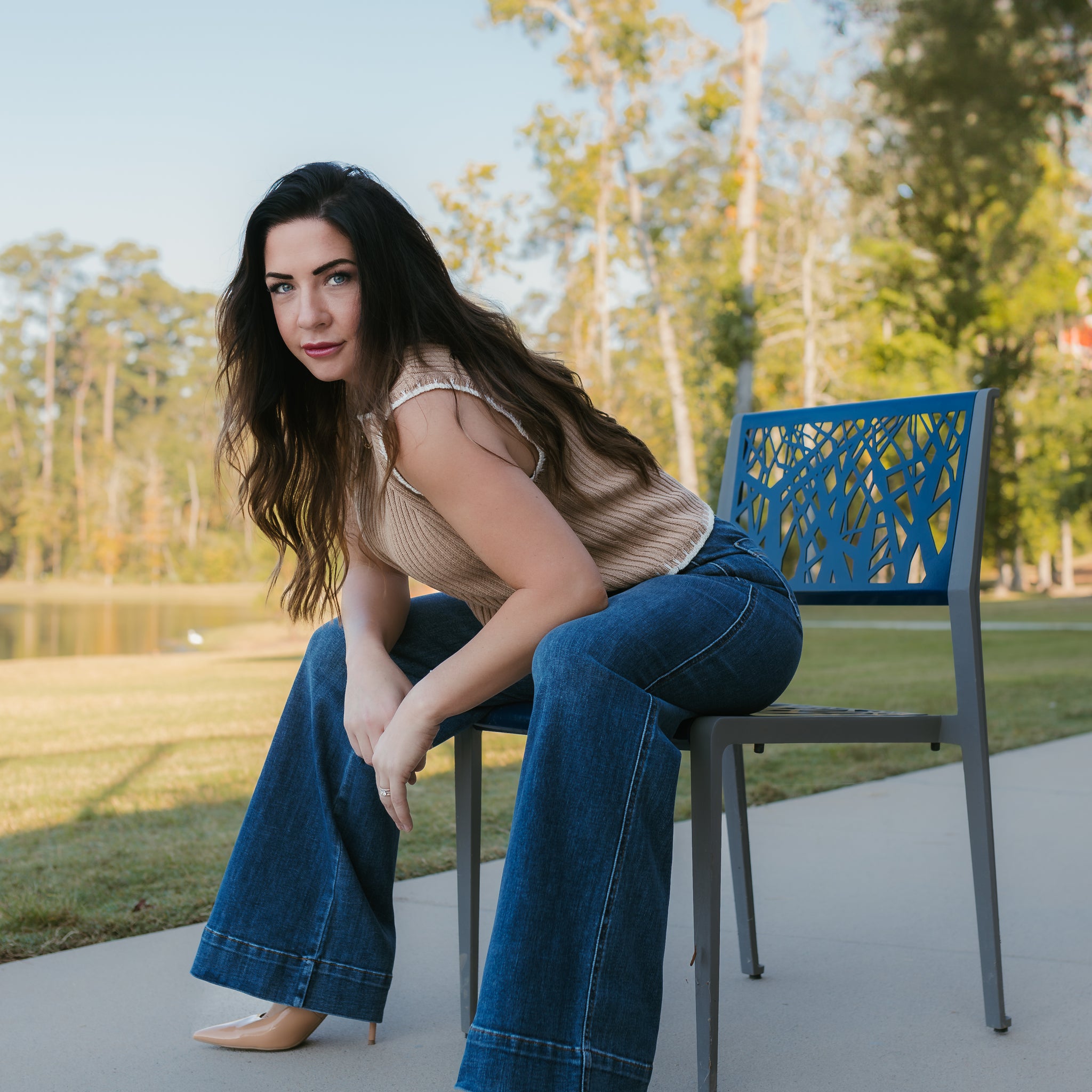 Woman sitting on a chair outdoors with trees and grass in the background. Stockbridge Styles Judy blue jeans and Stockbridge Styles sweater knit top