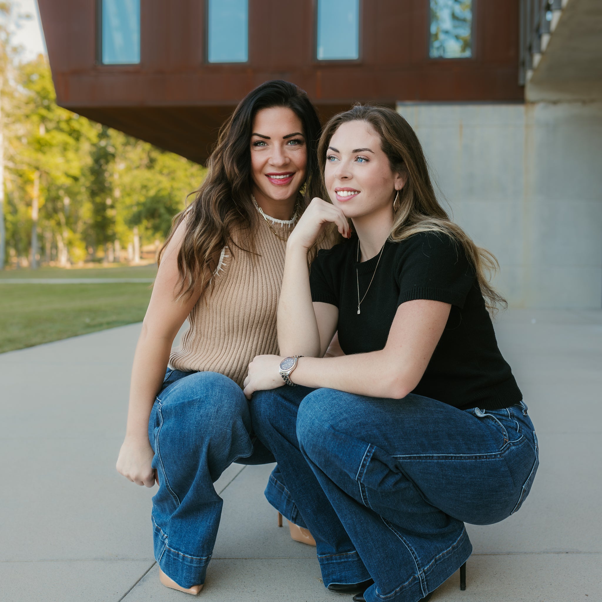 Two women sitting on a concrete surface with a modern building in the background. Stockbridge Styles clothing store 