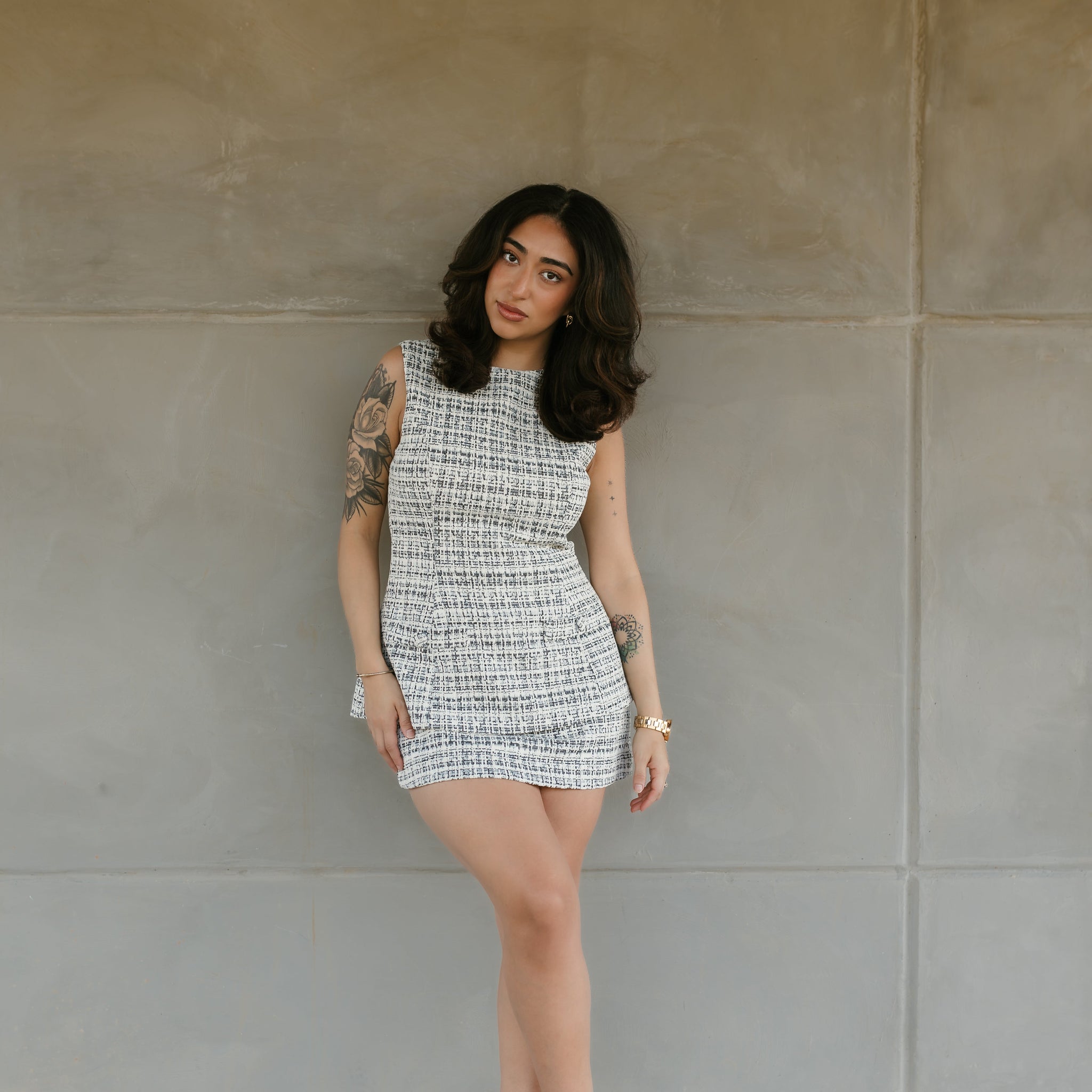 Woman in a patterned dress standing against a concrete wall. Stockbridge Styles tweed mini dress