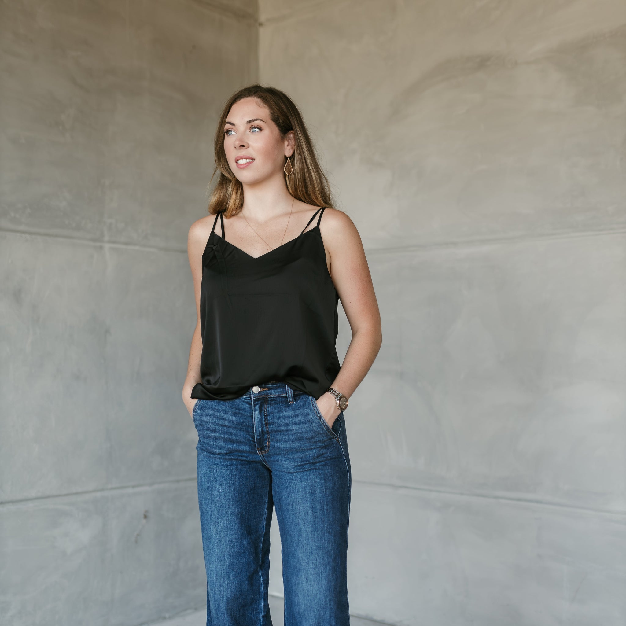 Woman wearing Stockbridge Styles black top and Judy  blue jeans standing against a plain wall. shop stockbridge styles