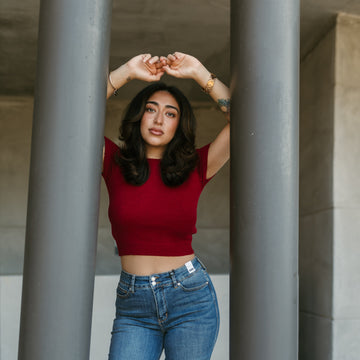 Woman in a red top and Judy blue jeans standing between two gray columns.