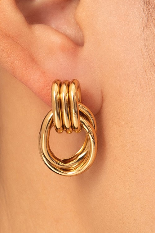 Gold hoop earring worn on an ear with a neutral background