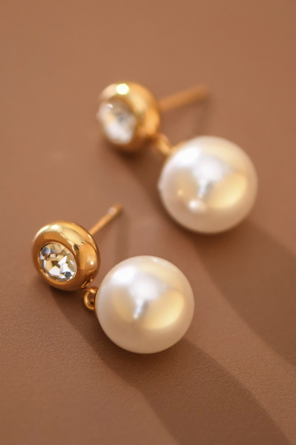 Pearl earrings with gold posts on a brown background