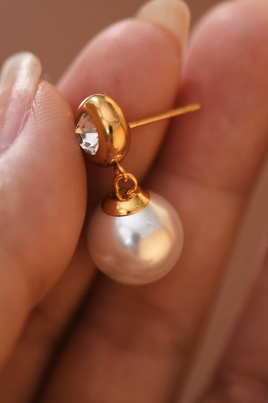 Gold earring with a pearl and clear gemstone held between fingers.
