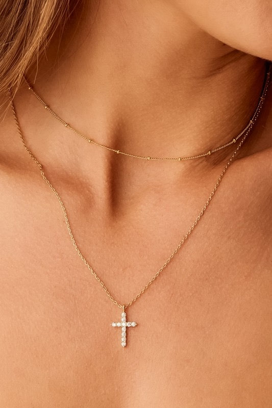 Close-up of a person wearing a gold necklace with a cross pendant on a light skin background