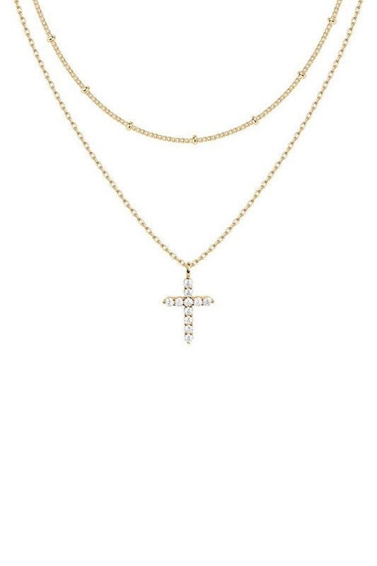 Close-up of a person wearing a gold necklace with a cross pendant on a light skin background