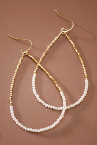 Gold and white beaded earrings on a brown background