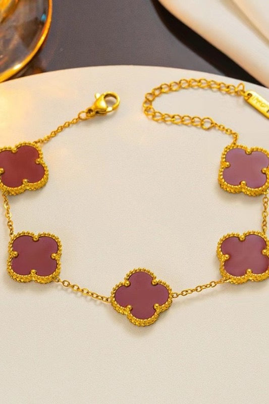 Gold bracelet with purple clover-shaped links on a beige surface