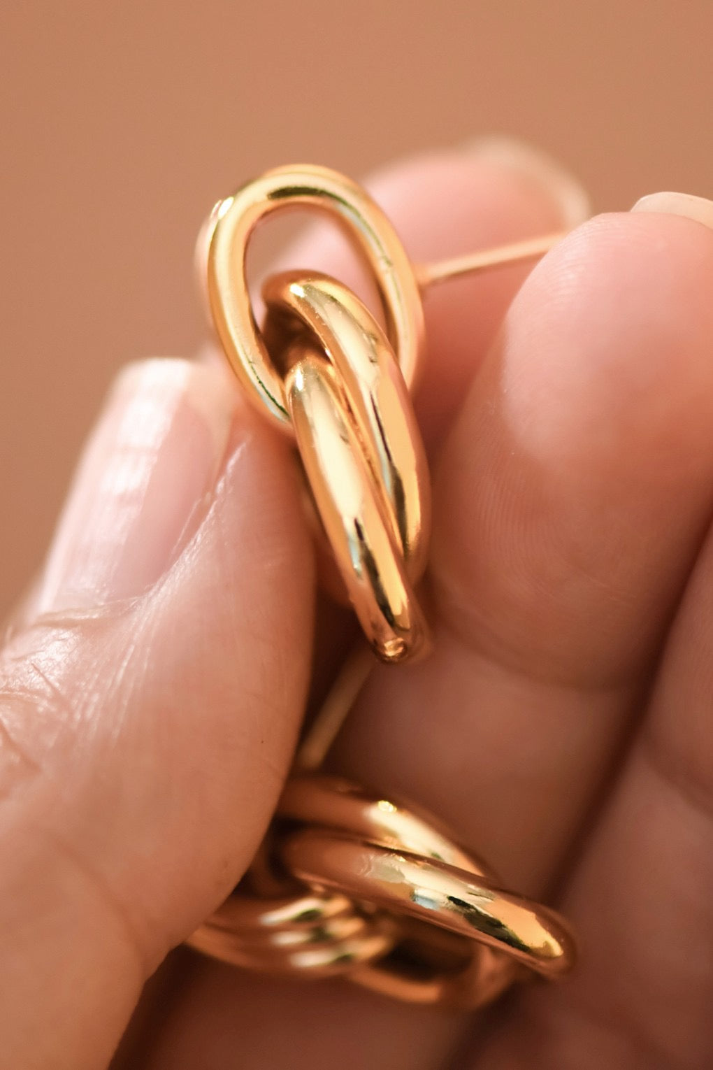Gold hoop earring worn on an ear with a neutral background